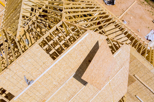 Workers are assembling wooden beams on roof plywood of new building in construction site