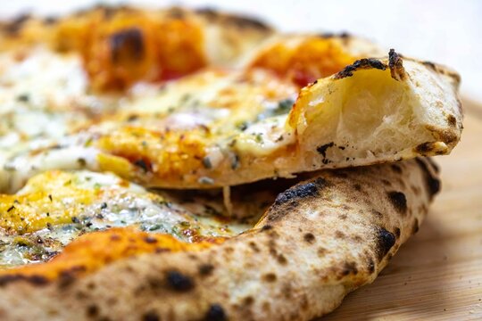 Neapolitan-style four-cheese pizza with leopard-spotted puffy crust and open airy crumb, sliced on a bamboo board &mdash; naturally leavened long-fermentation dough.