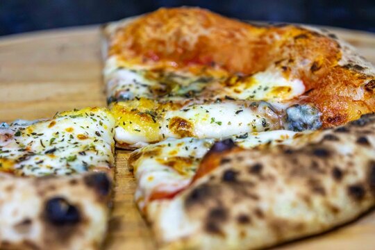 Neapolitan-style four-cheese pizza with leopard-spotted puffy crust and open airy crumb, sliced on a bamboo board &mdash; naturally leavened long-fermentation dough.