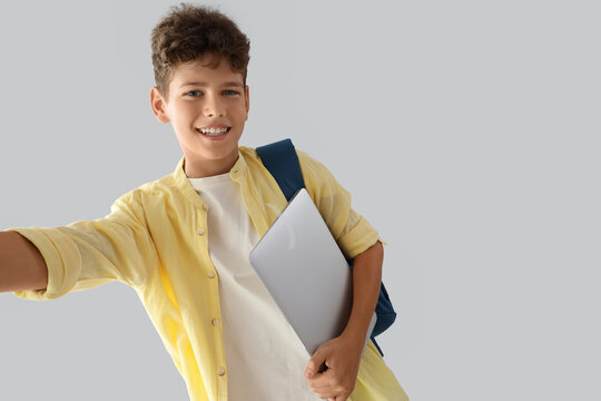 Digital education and modern learning, happy schoolboy with laptop and backpack taking a selfie on a light background
