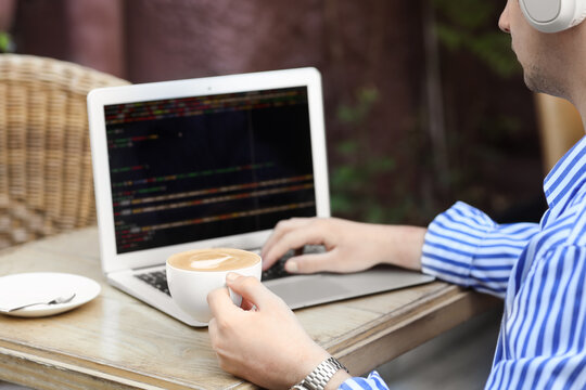 Male programmer working with laptop and coffee at table in street cafe, closeup