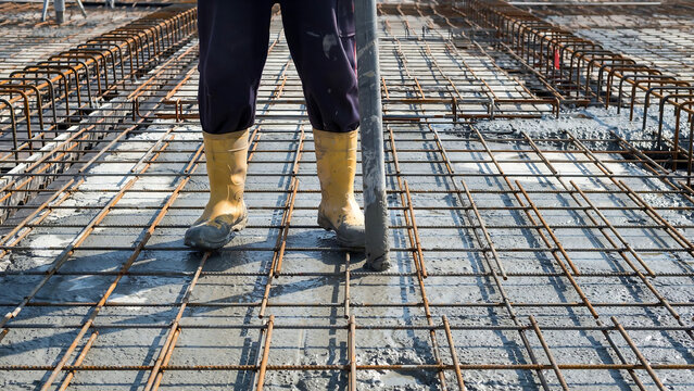 Construction worker smoothing wet concrete over rebar grid with a trowel during foundation work