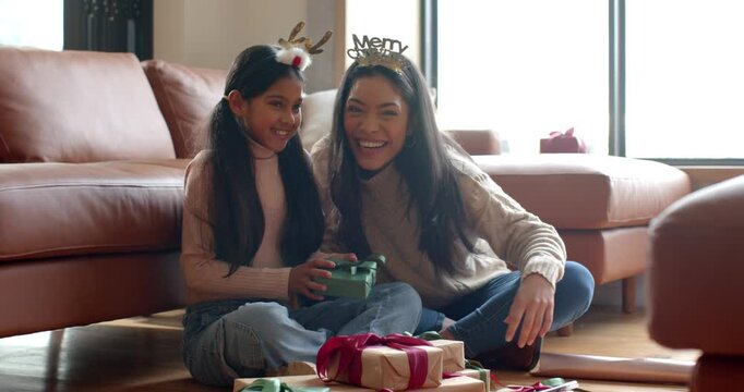 Diverse mother and daughter discovering green gift at home untying ribbon hugging celebrating joy