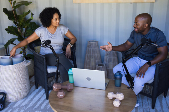 African American co-hosts in gym wear recording conversation in studio with laptop and boom mics