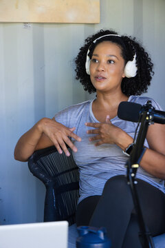African American woman speaking into black microphone while wearing white headphones in home studio