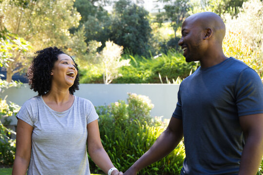 African American couple facing each other, laughing and holding hands in sunlit garden wristband