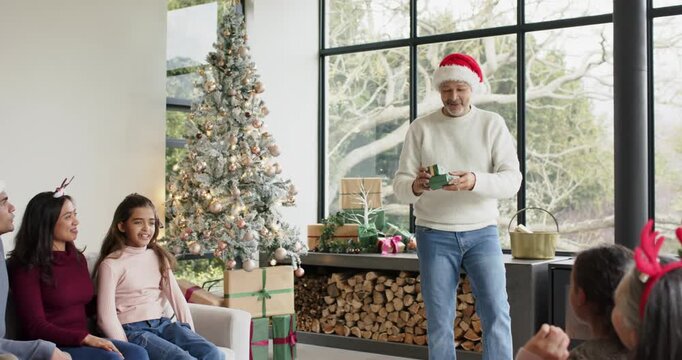 Father entering living room by Christmas tree holding present, handing daughter gift, copy space