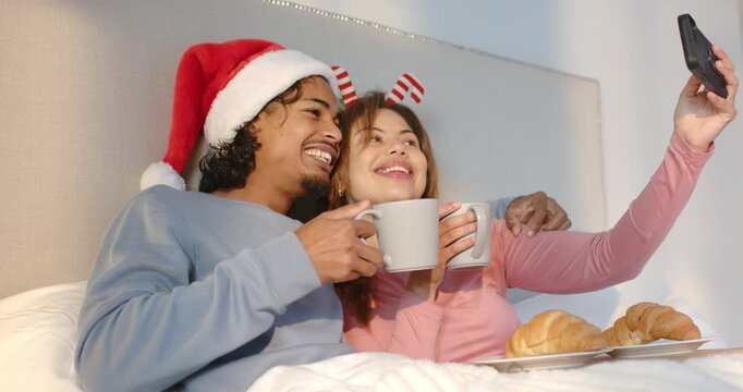 Couple holding tray taking smartphone selfie on bed toasting mugs and sipping to capture memory