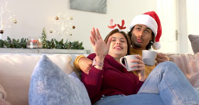 Leaning back Diverse couple wearing antlers holding mugs, laughing, pointing off camera, smiling