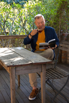 Weathered wooden table holding paperback and clear glass cup on porch, receiving dappled sunlight