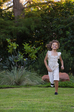 African American child girl running across manicured lawn at residential garden with stone bench