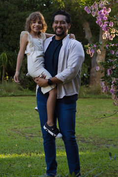 African American father holding daughter while smiling in garden showing wristwatch and shoes