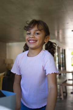 African American girl in pink top smiling and standing by table with blurred box at home