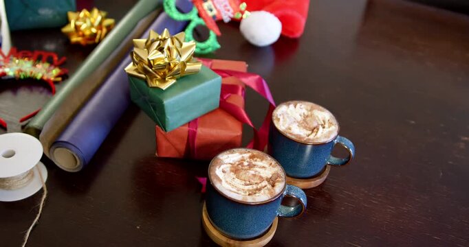 Camera is shifting left and upward to reveal wooden table with two mugs, gifts, wrapping supplies