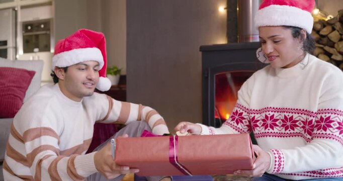 Couple wearing Santa hats starting tying ribbon on rug, wrapping gifts and writing tags for holiday