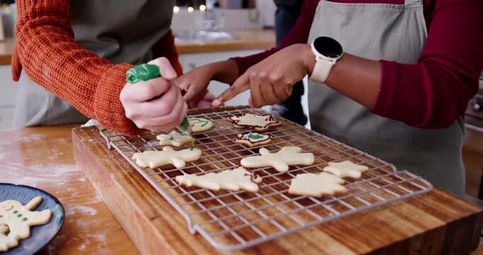 Diverse female friends at home starting green-icing outlines and piping holiday cookies on rack