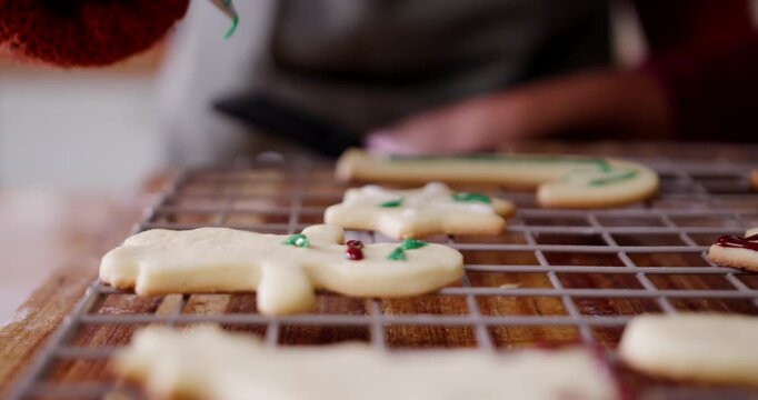 Diverse friends decorating fresh ginger cookies home with green piping bag on rack for holiday