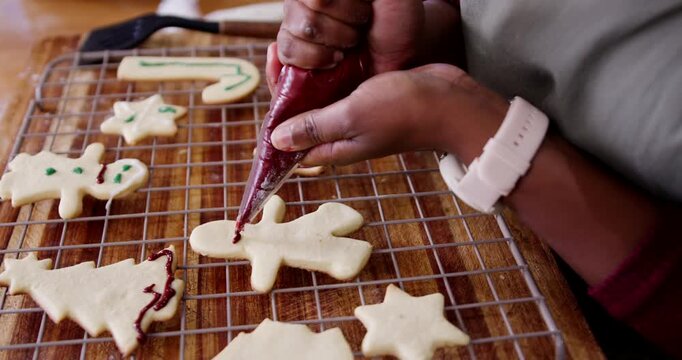 Adult African woman squeezing red piping bag, outlining gingerbread on cooling rack for holidays