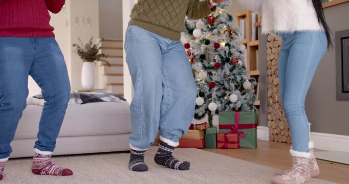 African American family dancing with teen in living room prompted by Xmas tree in Santa hats