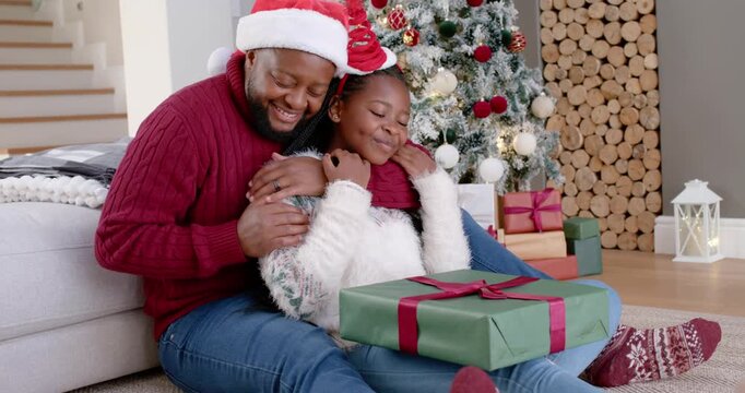 African American dad and daughter sitting at home, green gift encouraging inspecting for opening