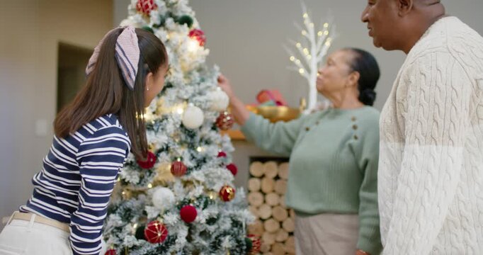 African American senior couple guiding teenage girl decorating pre-lit tree at home, placing topper