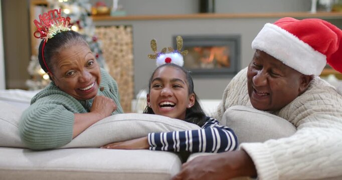 African American family sharing looks and laughing on couch with Santa hat near Christmas tree