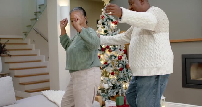 Senior woman, mature man dancing in living room to holiday music by Christmas tree and gifts