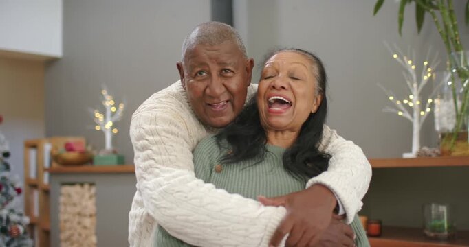 African American couple mature man approaching from behind, hugging senior woman by stove, laughing