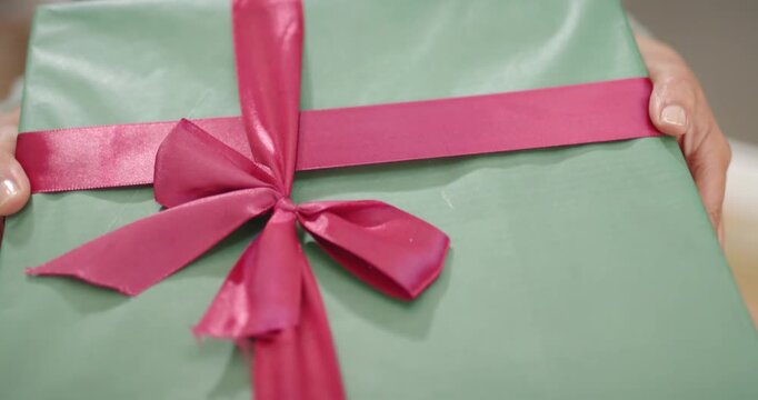 Camera is pulling back as hands are tilting and pushing green gift toward camera, revealing tree