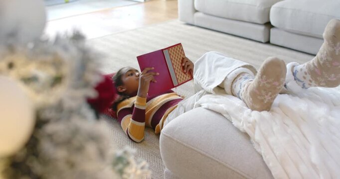 Red book sliding behind ottoman revealing African American schoolgirl propping legs and reading