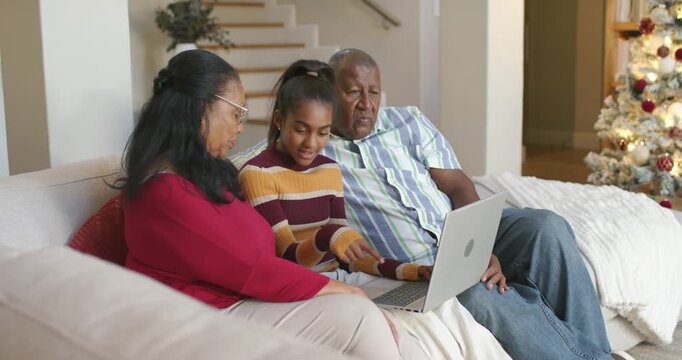 African American seniors with teen on couch teen starting typing on laptop grandparents helping