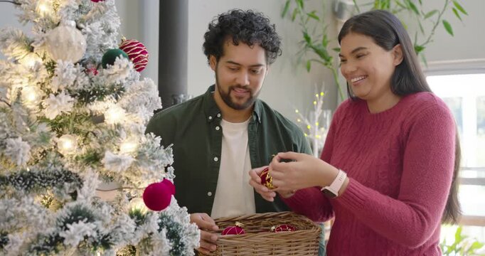 African American couple decorating frosted tree, man holding basket while woman hanging ornaments