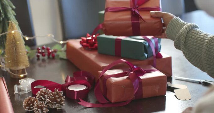 Hand entering frame is picking gift, placing and aligning on teal box, completing stack on table