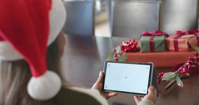 At dining table, woman is adjusting tablet and holding screen as camera is shifting, framing gifts