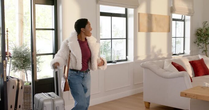 African American woman opening door pulling luggage removing fuzzy coat settling home by Xmas tree