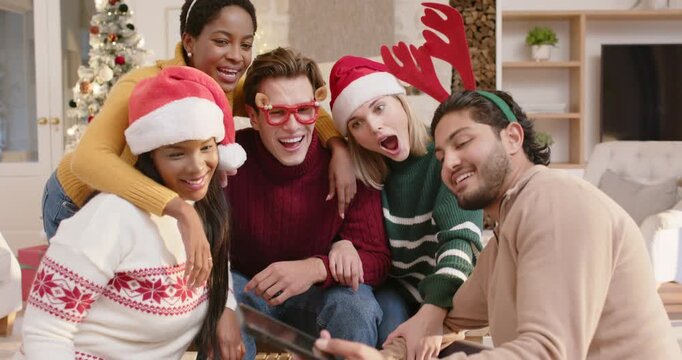 Diverse friends taking selfie on couch, man on right showing phone to check shot, everyone laughing