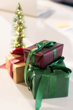 Three gift boxes sitting on tabletop beside Christmas tree, glowing with golden lights