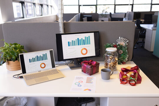 Office desk featuring laptop and monitor displaying colorful charts with gift boxes and wreath