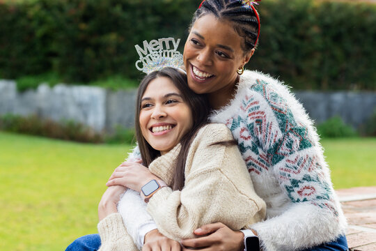 Mother and daughter hugging on brick ledge in garden wearing knit sweaters and Christmas headbands