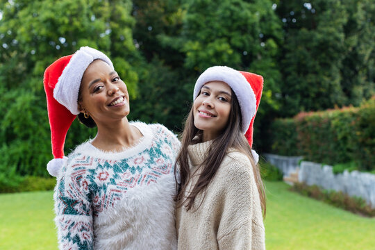 Standing in yard, Diverse family wearing Santa hats, Christmas and knit turtleneck sweaters smiling