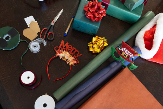 Wrapping paper rolls and ribbons are being scattered on dark wooden table with teal gifts, headband