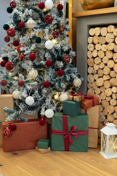 Flocked Christmas tree is standing left of living area with wrapped gifts, stacked firewood nearby
