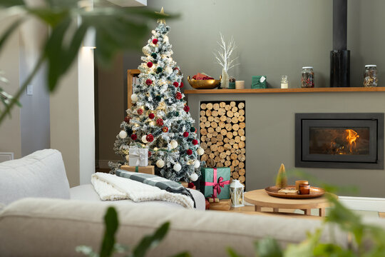 Flocked Christmas tree glowing with red and white ornaments, wrapped gifts, fireplace and sofa