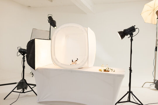 Collapsible pop-up light tent is sitting on white table in studio, with small bottles and softboxes
