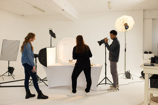 Diverse photography team adjusting camera and arranging products inside light tent in studio