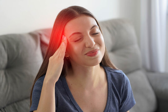 Young Latina woman touching her temples while suffering from severe migraine with red pain highlight