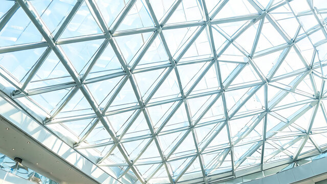 A modern geometric glass and metal grid roof structure, forming a skylight in an indoor public building space.