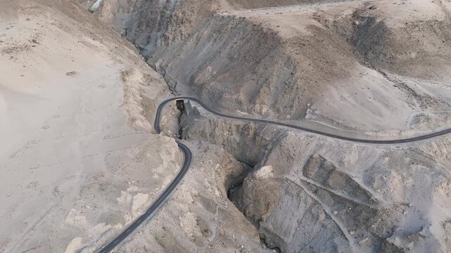 Aerial orbit shot of sharp s-curve on karakoram highway in the arid landscape and eroded mountains, cinematic drone reveal of the endless himalayan road