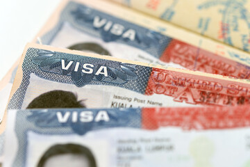 Naklejka premium Three United States visa stamp inside an open passport document, held by a hand, for immigration, international travel, border security, visa application, and citizenship topics.