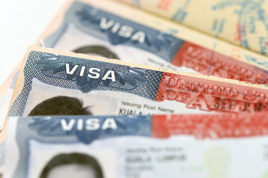 Three United States visa stamp inside an open passport document, held by a hand, for immigration, international travel, border security, visa application, and citizenship topics.